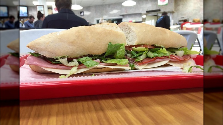 An Italian sub on a soft roll with thin layers of deli meats and cheese, topped with lettuce and tomato on a red plate