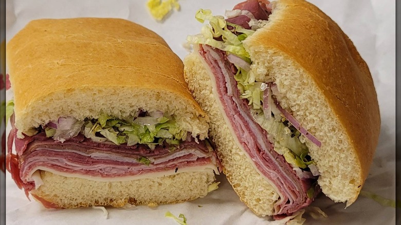 A thick-cut Italian sub sliced in half, stacked with layers of deli meats and cheese, topped with shredded lettuce and onions on a soft roll