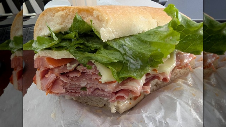 A close-up of an Italian sub loaded with deli meat, cheese, and lettuce on a soft roll