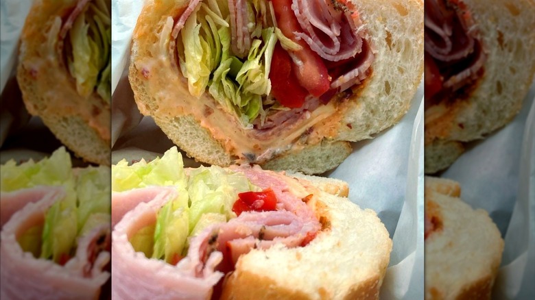 A close-up cross-section of an Italian sub with deli meats, lettuce, tomato, and mayo packed tightly inside a soft roll