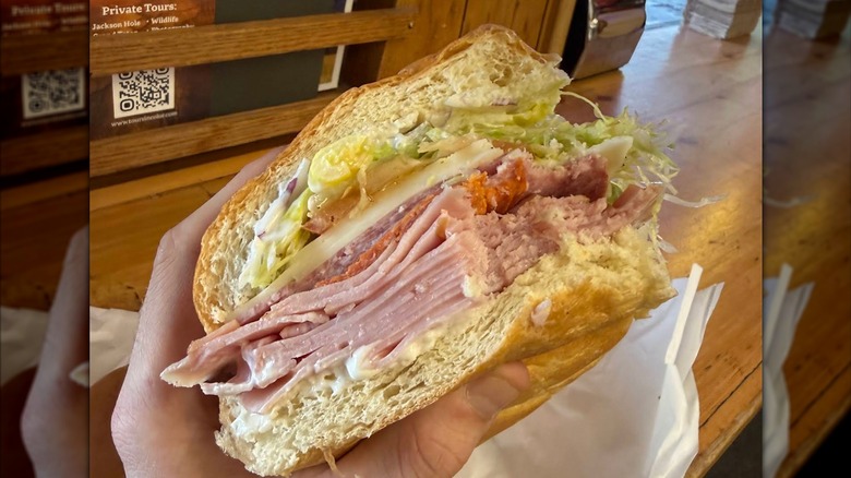 A handheld Italian sub with thick layers of deli meats and cheese, topped with shredded lettuce