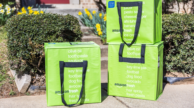 Amazon Fresh bags stacked at the bottom of stone steps leading up to a front porch with a red door.