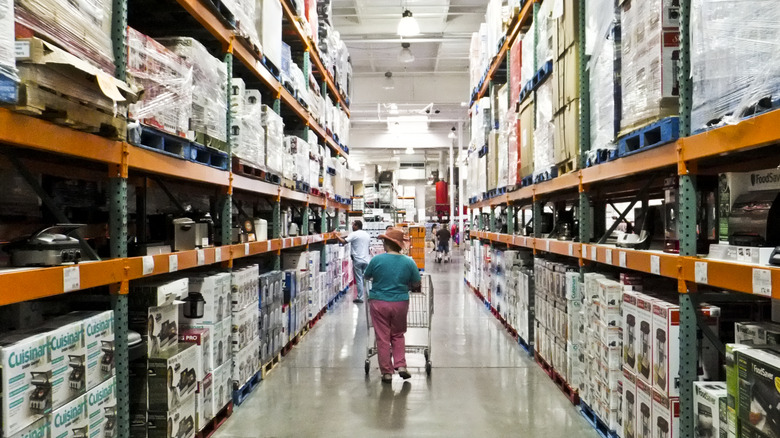 A shopper checks out products as they push a cart down an aisle in Costco.