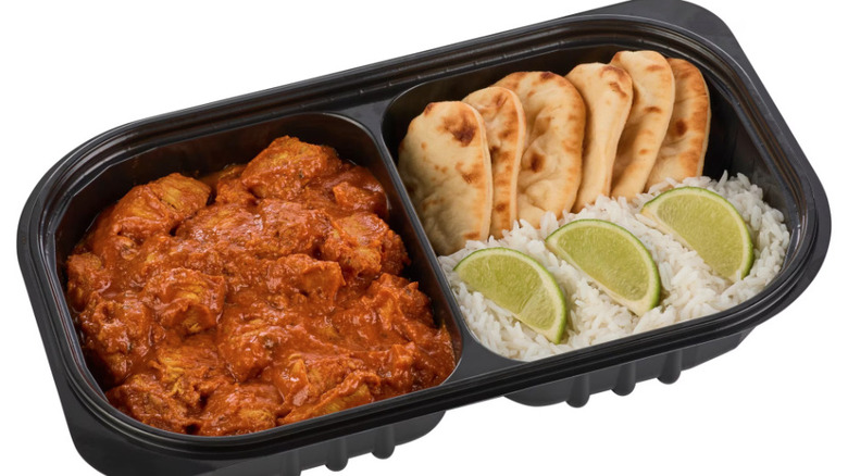 Plastic container of chicken tikka masala with rice, naan, lime slices