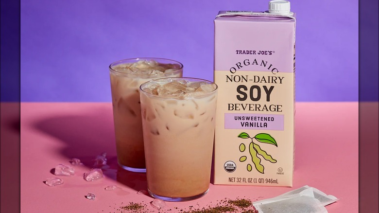 Small carton of organic soy beverage on table next to two glasses containing the beverage and ice.