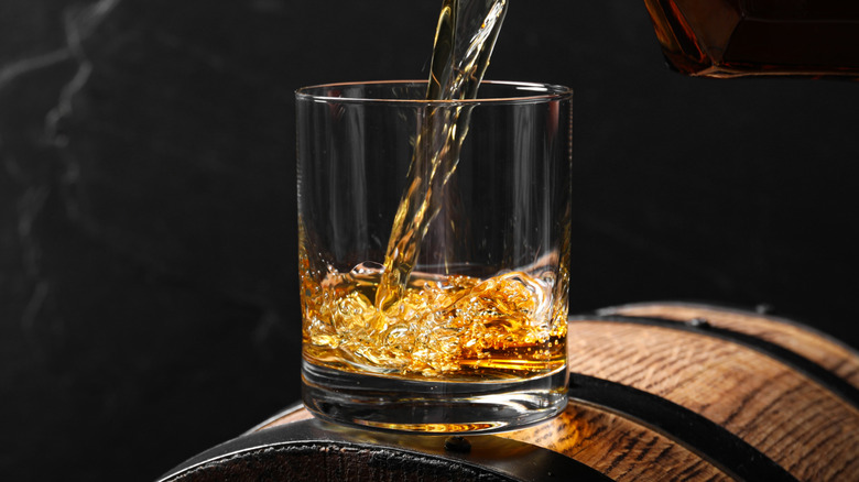 Pouring bourbon into glass tumbler on top of a barrel