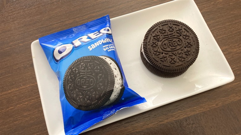 A sealed Oreo sandwich frozen dairy dessert next to an open one on a white rectangular plate.