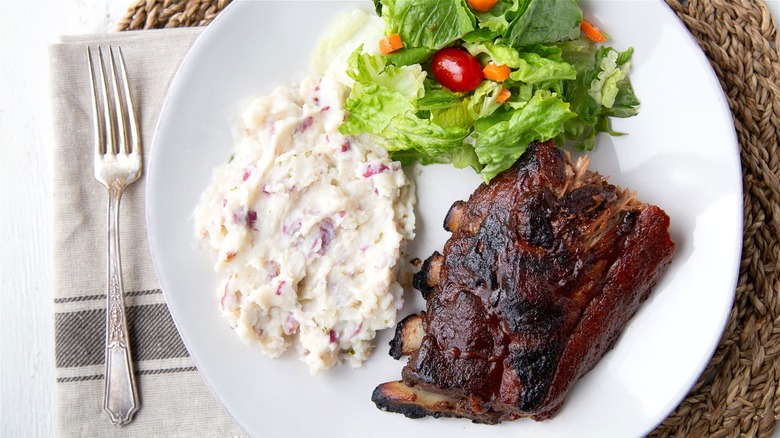 A plate of tender baby back ribs served with mashed potatoes and a side salad.