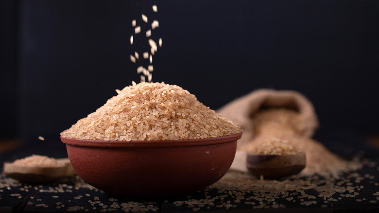 Dry brown rice in a clay bowl surrounded by more rice