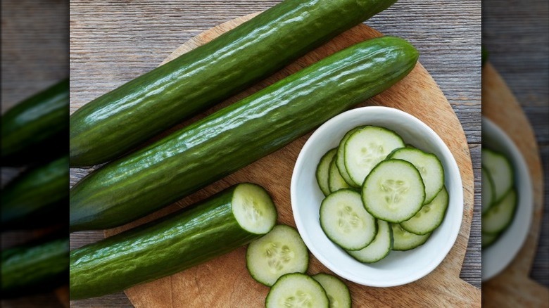 A three-pack of English cucumbers with one half-sliced and slices sitting in white bowl.