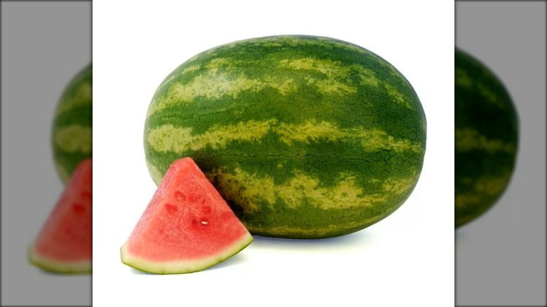 Whole intact watermelon with a single triangular slice in the foreground.