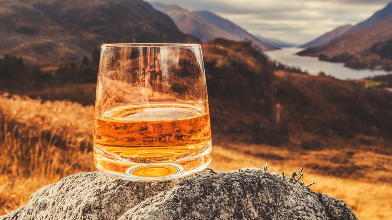 Glass of Scotch on rock in Scottish Highlands.