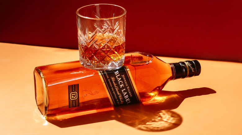 Glass of whisky on bottle of Johnnie Walker Black Label laid on its side.