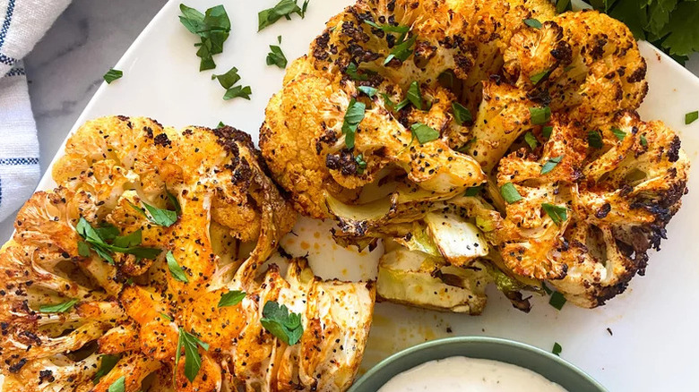 two cauliflower steaks on a white plate with sauce at the bottom edge