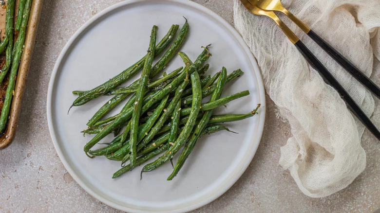 roasted green beans on a white plate with gold and black flatware