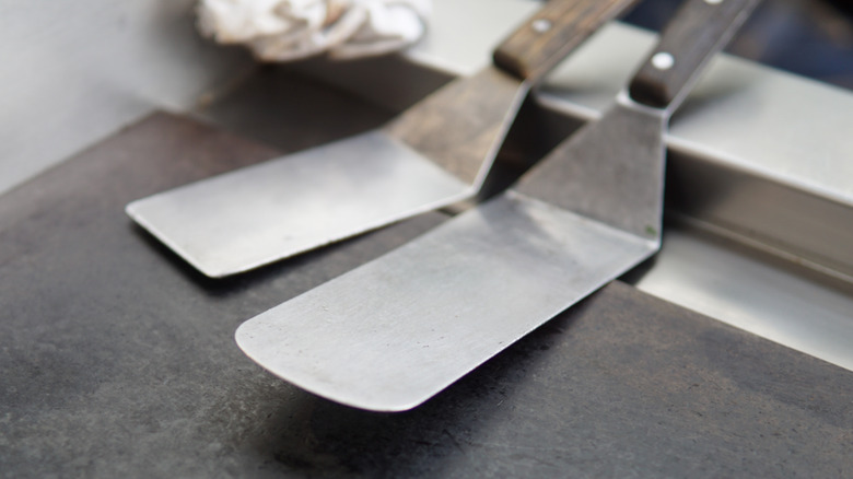 Two metal spatulas with wooden handles on flat-top grill.
