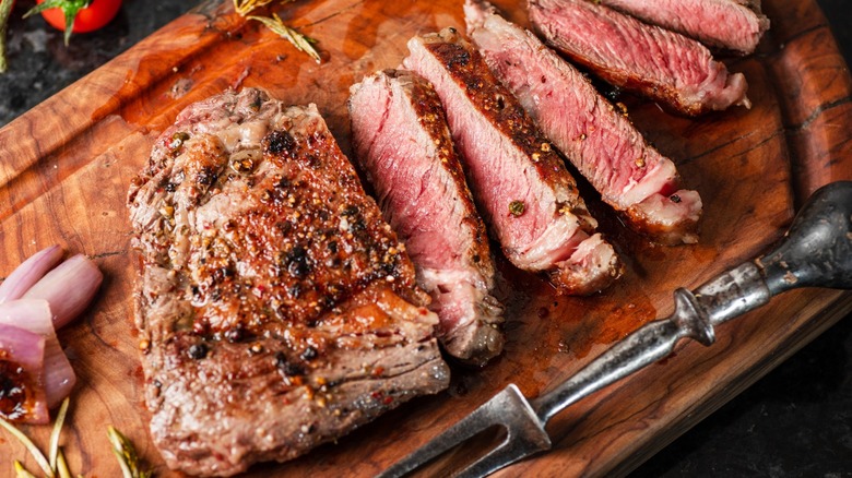 Grilled, sliced steak on a wooden cutting board.
