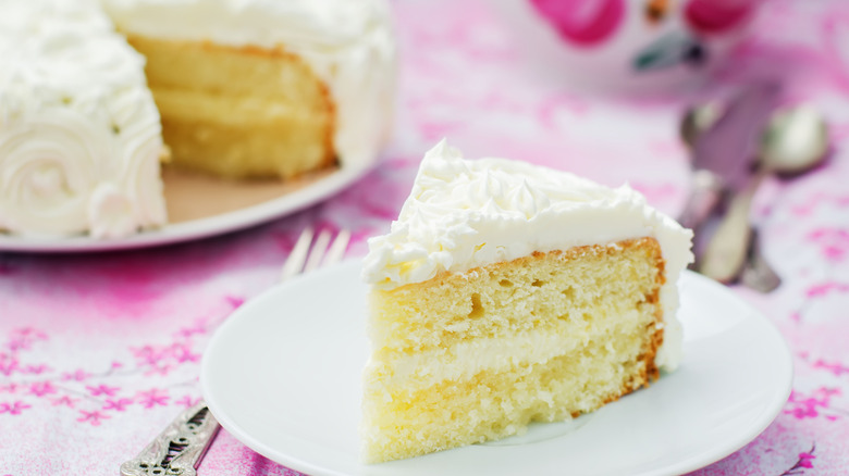 Slice of vanilla cake with white icing on a white plate