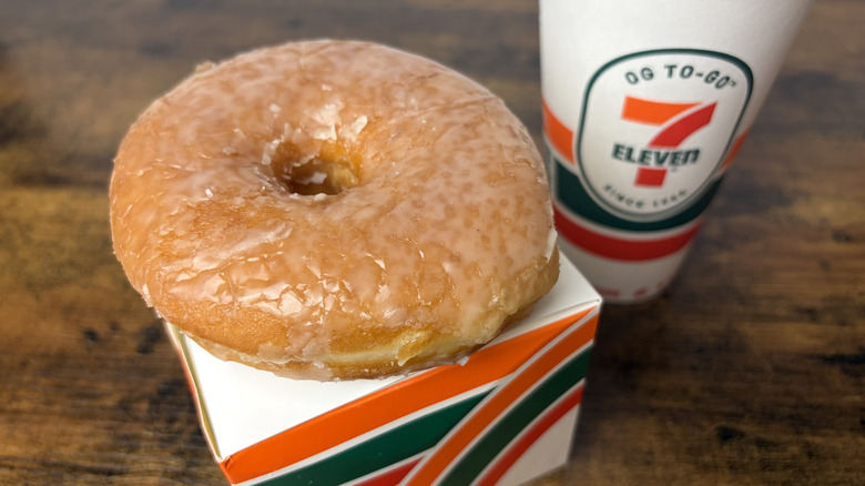 A 7-Eleven Glazed Donut on top of donut box next to takeout cup