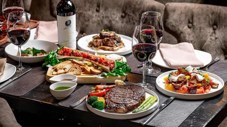 A restaurant table with steak, bone marrow, and glasses of red wine