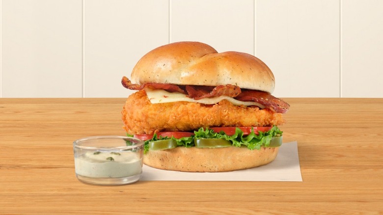 Chick-fil-A's jalapeño ranch club sandwich on table next to glass cup of dressing.