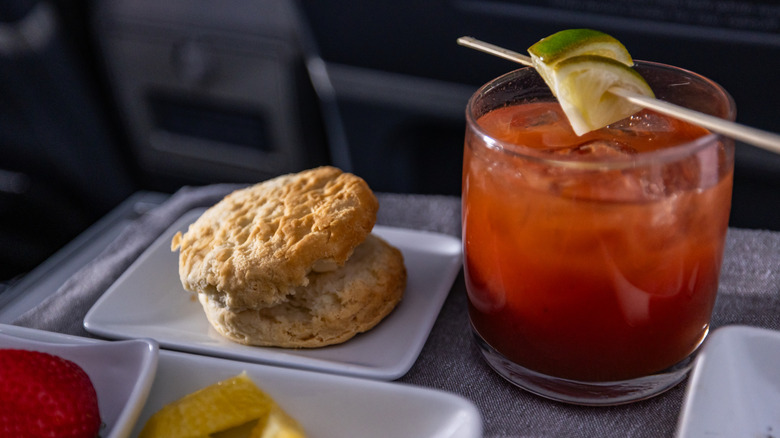 A Bloody Mary cocktail and breakfast sandwich on a plane seat tray.