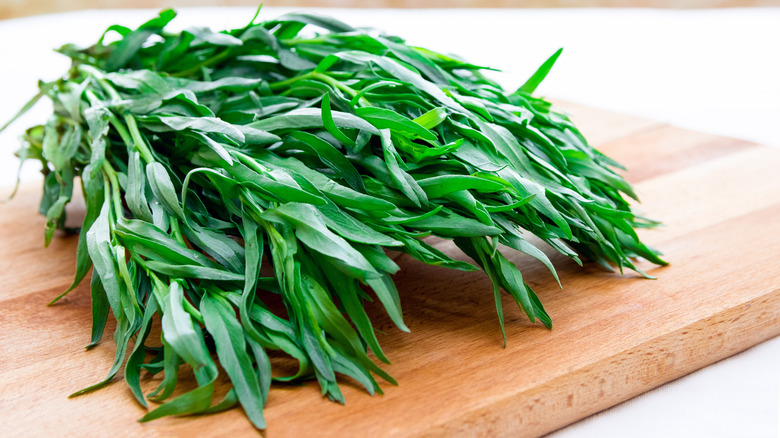 A stack of fresh tarragon sprigs on a wooden cutting board