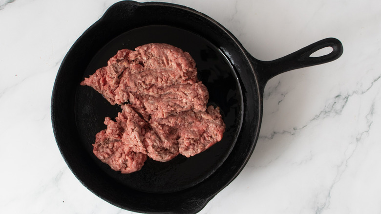 raw ground beef in a black frying pan