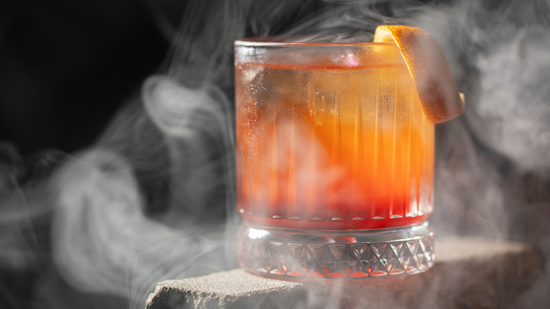 A smokey old-fashioned cocktail garnished with an orange twist
