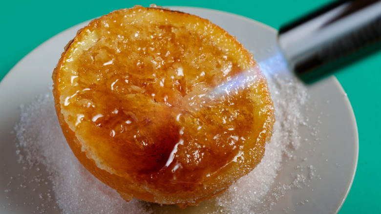 Closeup of a kitchen blowtorch used to caramelize an orange slice with white sugar