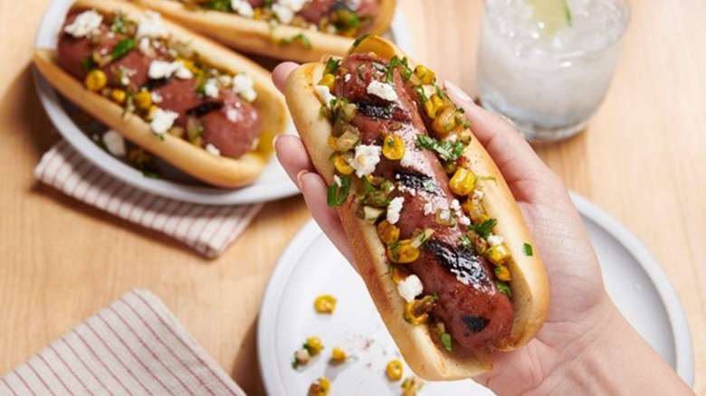 hand holding beyond sausage in bun with toppings