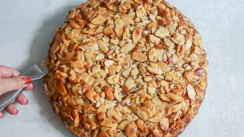 Knife slicing through almond-topped cake