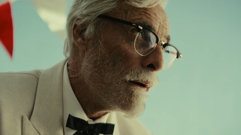 Screenshot of Colonel Sanders in glasses, suit, and bow tie with serious expression looking up in a KFC 2025 promotion video, "Obsession"