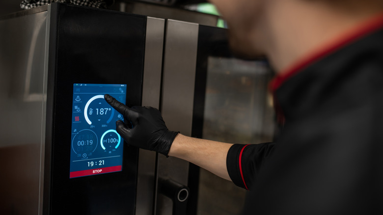 A chef tapping on a touchscreen to adjust oven temperature and timer inside an industrial kitchen