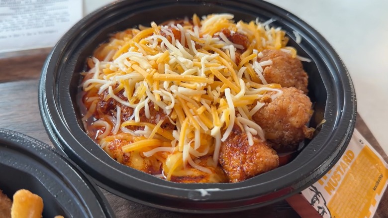 A closeup of KFC mac & cheese $5 bowl, with shredded cheese and fried chicken nuggets, next to sauce packet of honey mustard