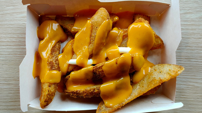 Top view of a takeout box of KFC potato wedges drizzled in cheese sauce