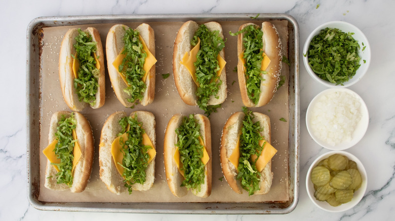 Hot dog buns filled with cheese and lettuce next to bowls of toppings