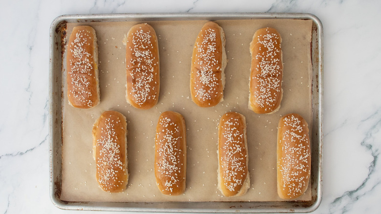 Sesame seed hot dog buns on baking sheet