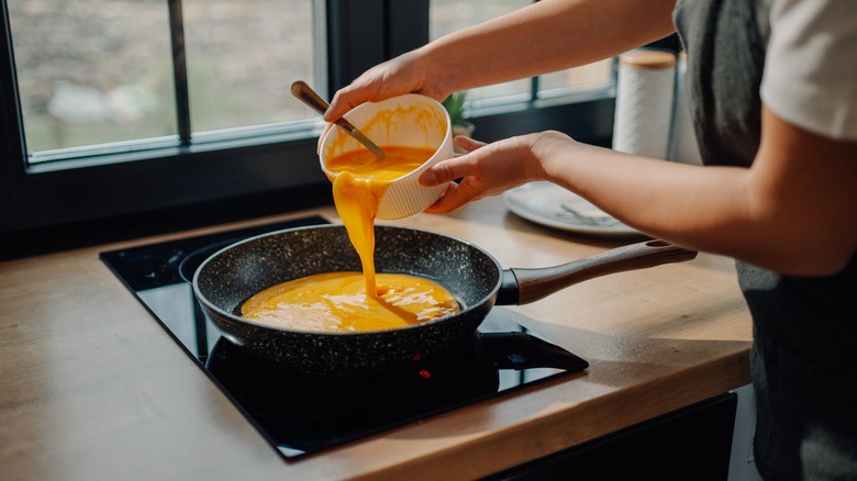 person pouring eggs into pan