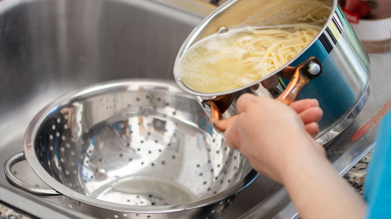 hands pouring pasta into colander