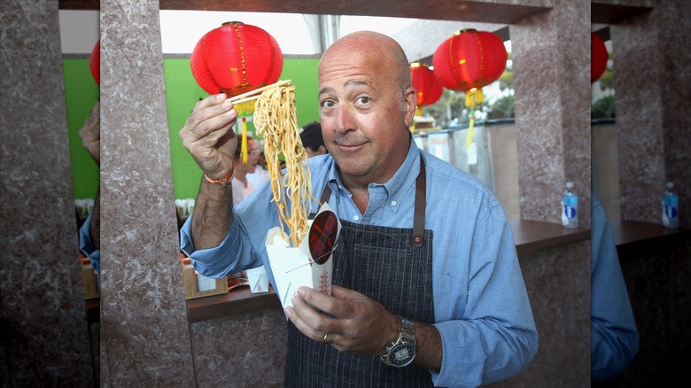 Andrew Zimmern eating noodles with chopsticks at a pop-up event
