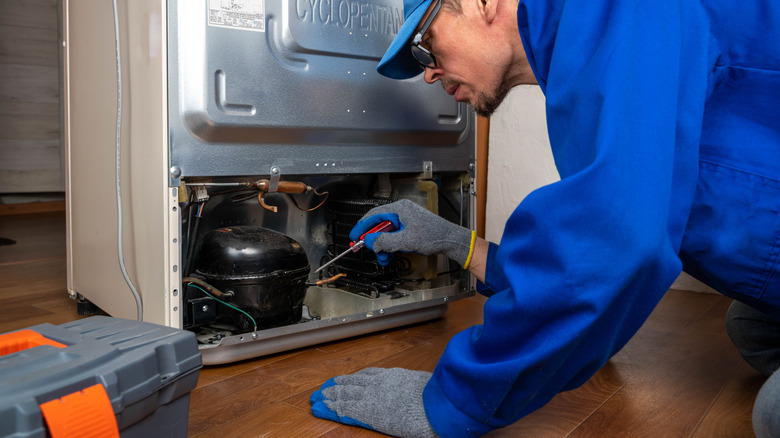 Repair man examining a refrigerator compressor