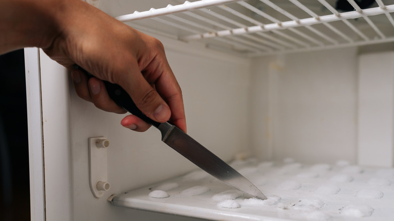 Person scraping off frost in freezer with a knife.