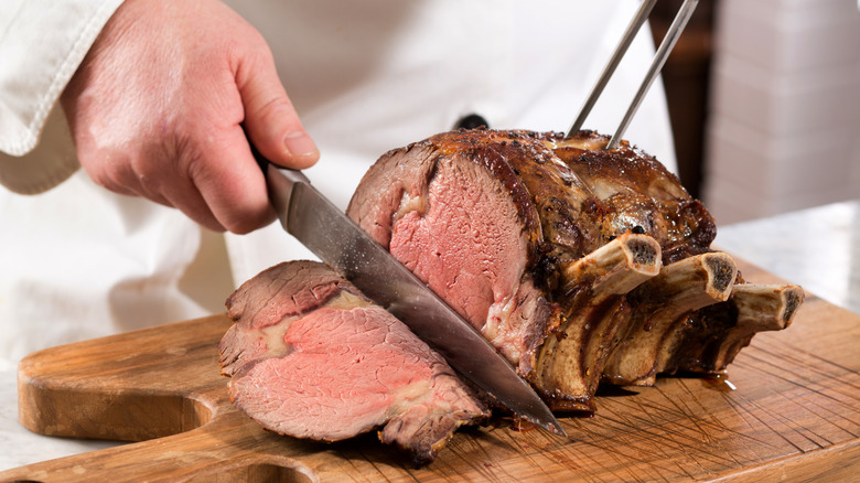 Male hand carving prime rib on a cutting board