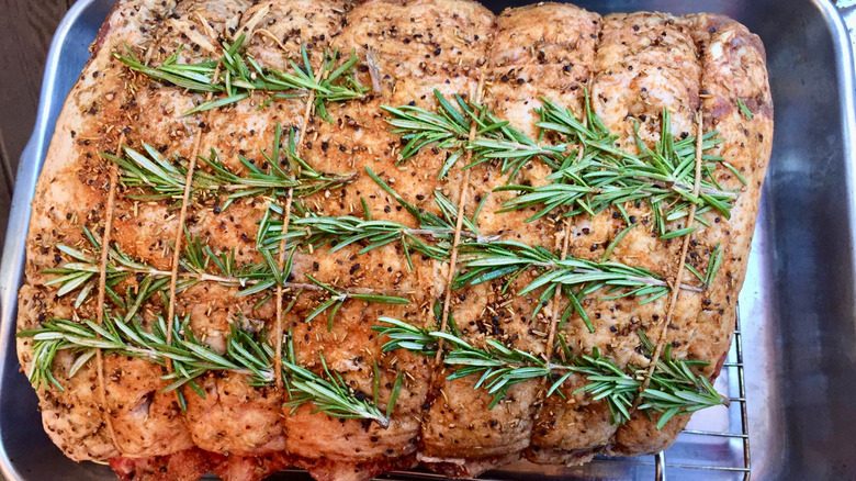 Raw prime rib tied with twine and seasoned with seasonings and rosemary
