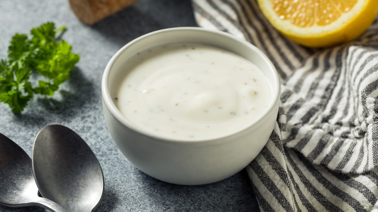 Small bowl of ranch dressing on table with utensils and ingredients