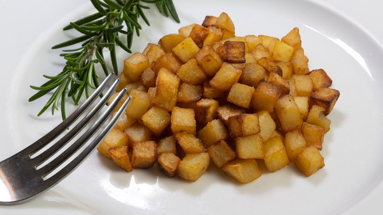 Cubed hash browns on white plate with metal fork and garnish