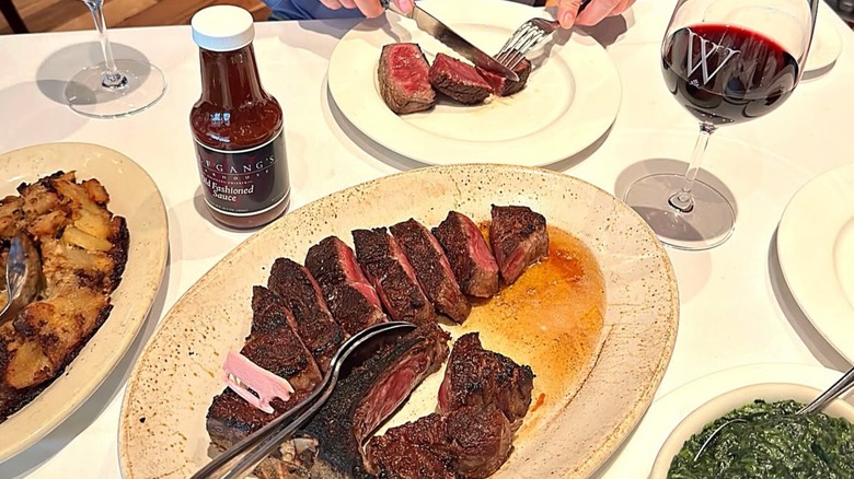 Sliced porterhouse steak from Wolfgang's with potatoes, creamed spinach, and a glass of red wine
