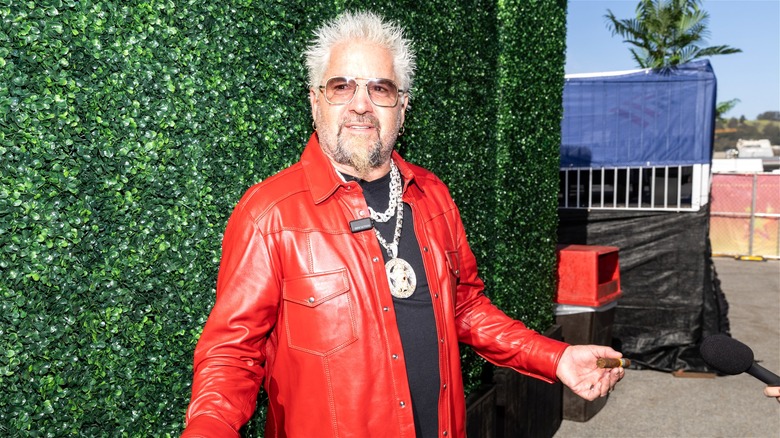 Guy Fieri, dressed in a red leather jacket, posing for photos at an event.