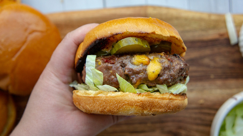 a beef burger with pickles, cheese, and lettuce held in a hand